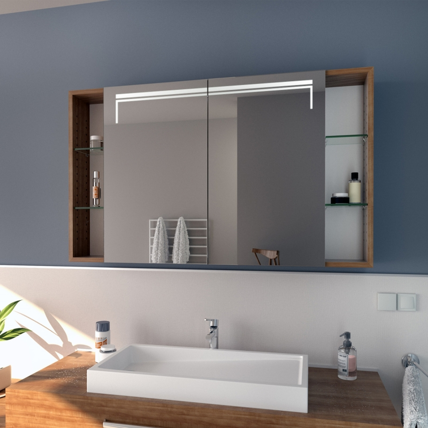 GRIMSTAD Spiegelschrank in Seitenansicht mit eingeschalteter Beleuchtung, 1500x1500 mm, warmweißes LED-Licht, zweitürig mit offenen Holzseitenfächern, über Holzwaschtisch mit weißem rechteckigem Aufsatzwaschbecken, blaue Wand, modernes Bad mit Grünpflanze