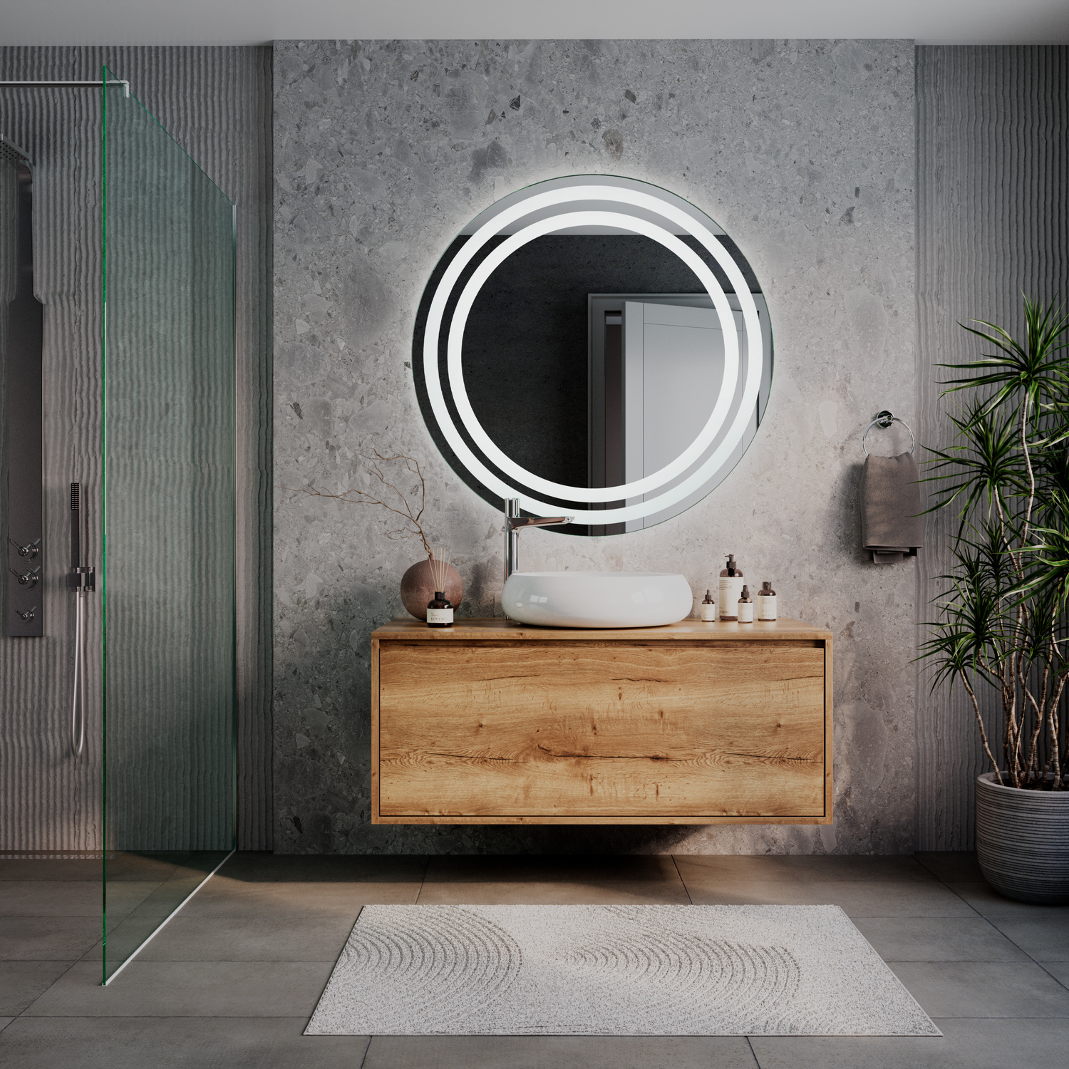 AMOR runder LED-Kosmetikspiegel mit eingeschalteter Beleuchtung, 1500x1500 mm, leuchtend mit warmweißem Lichtring, freistehend auf modernem Holzwaschtisch, elegantes Bad mit grauer Betonwand, grüner Glastrennwand und Pflanze